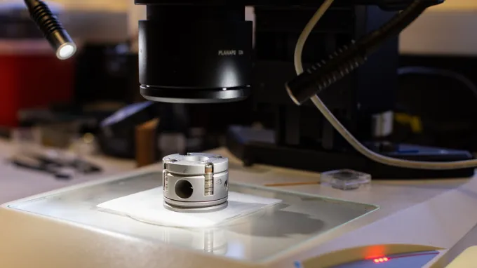 A small, cylindrical object is illuminated beneath a microscope
