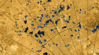 A satellite view of the surface of Titan from the Cassini spacecraft shows multiple lakes scattered across the moon's yellow surface. Latitude and longitude lines are shown in black.