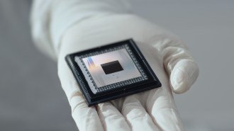 A gloved hand holds a shiny metallic quantum computing chip.